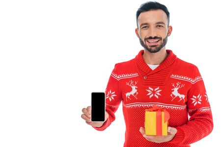 happy man in sweater pointing with finger at smartphone isolated on whiteの写真素材