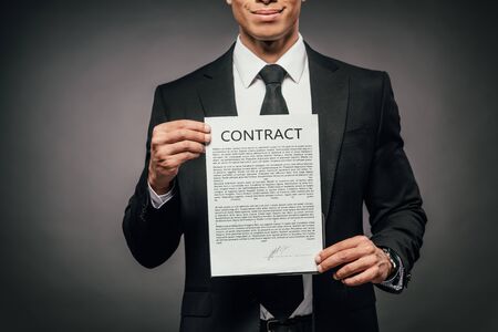 partial view of cheerful african american businessman showing contract on dark background