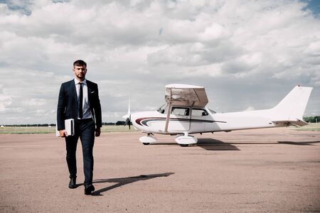 full length view of businessman in formal wear holding laptop and map in sunny day