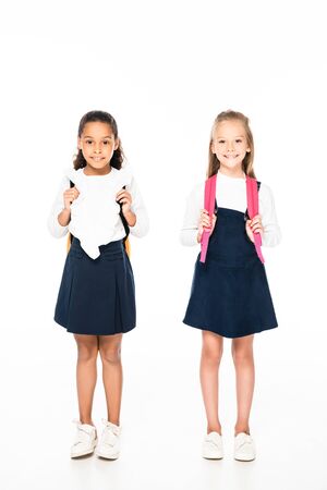 full length view of two adorable multicultural schoolgirls smiling at camera on white backgroundの写真素材