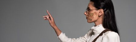 panoramic shot of steampunk woman in glasses looking away and gesturing isolated on greyの写真素材