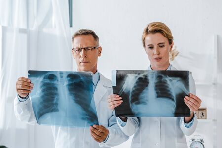 doctor in glasses and attractive coworker looking at x-rays in clinic