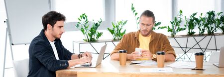 panoramic shot of two handsome friends using laptop and smartphone