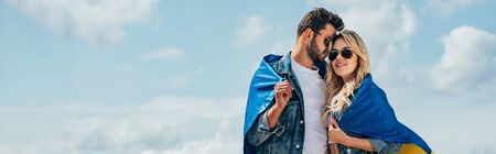 panoramic shot of attractive woman and handsome man smiling and holding ukrainian flag