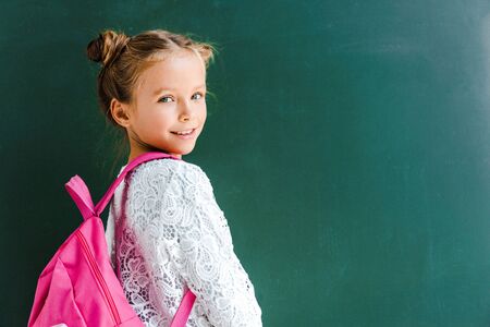 happy schoolkid smiling while standing with backpack on green