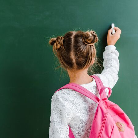 back view of kid holding chalk near chalkboard on greenの写真素材