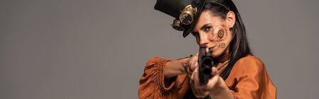 panoramic shot of focused steampunk woman aiming with pistol at camera isolated on grey