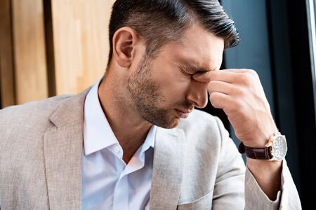 tired businessman touching nose with closed eyes in cafeの写真素材