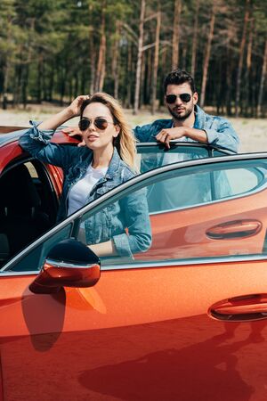 attractive woman and handsome man in jackets standing near car