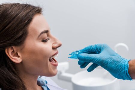cropped view of dentist in latex glove holding retainer near cheerful girl