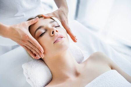 cropped view of masseur doing face massage to attractive woman