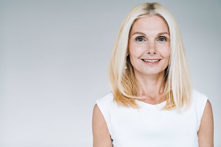 happy blonde mature woman smiling isolated on grey