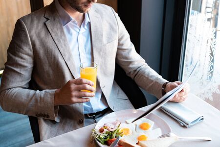 cropped view of businessman holding glass of orange juice and newspaper in cafeの写真素材
