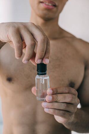 selective focus of muscular mixed race man opening bottle with cosmetic serumの写真素材