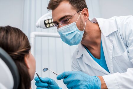 selective focus of dentist in medical mask holding dental instruments near patient