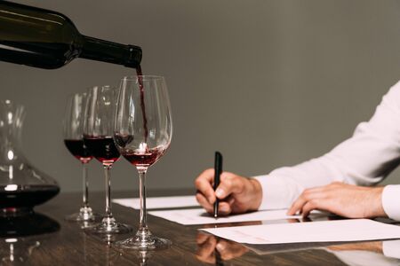 partial view of sommelier writing at table with wine glasses