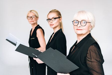fashionable three-generation businesswomen in glasses with folders isolated on greyの写真素材