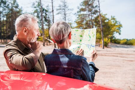 seniour couple of tourists standing near red car and looking at mapの写真素材