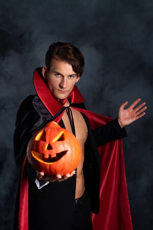 handsome man holding halloween pumpkin and gesturing on black with smokeの写真素材