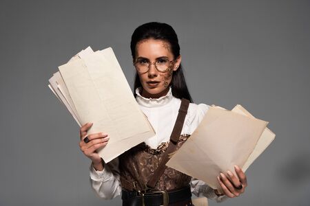 attractive steampunk woman in glasses holding documents and looking at camera on greyの写真素材
