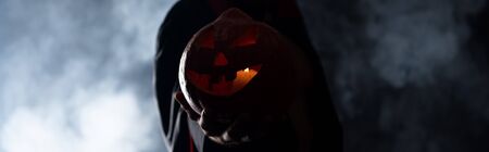 panoramic shot of man holding pumpkin on black with smokeの写真素材