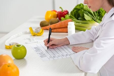 cropped view of dietitian writing in meal plan at workplaceの写真素材