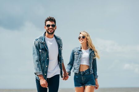 attractive woman and handsome man in denim jackets smiling and holding hands outsideの写真素材