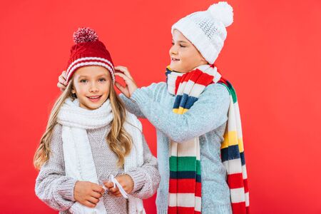 two smiling kids in winter outfits isolated on redの写真素材