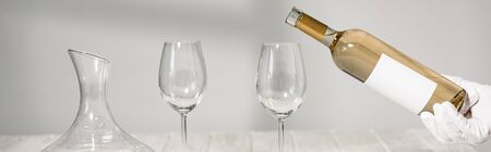 panoramic shot of waiter in white glove pouring wine in wine glasses