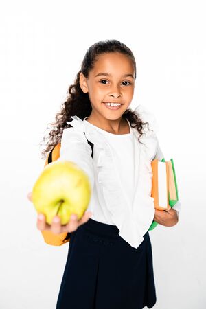 selective focus of african american schoolgirl showing apple while holding books on white backgroundの写真素材