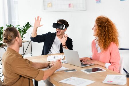smiling businessman with virtual reality showing hands and friends looking at him