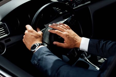 cropped view of african american businessman in suit beeping in car at sunny day