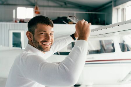 smiling bearded man standing near plane and holding sunglassesの写真素材
