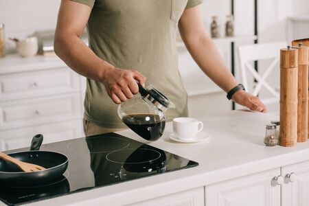 partial view of asian man pouring coffee in cup while standing near cooking surface in kitchenの写真素材