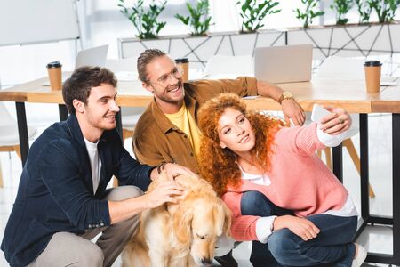 three smiling friends taking selfie with cute golden retriever
