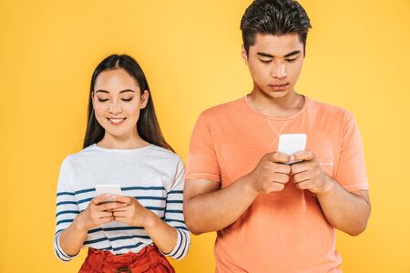 young asian man and woman using smartphones isolated on yellow