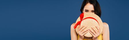 panoramic shot of pretty girl holding straw hat isolated on blueの写真素材