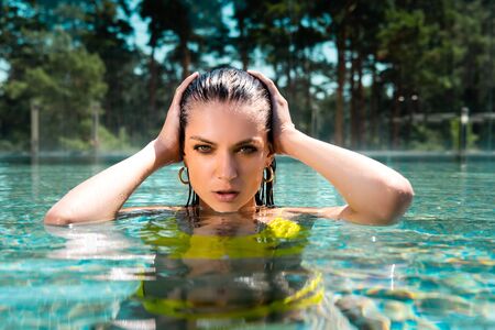 beautiful sexy woman in swimming suit with hands on head posing in pool on resort