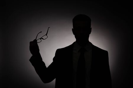 black silhouette of businessman holding glasses with back lightの写真素材
