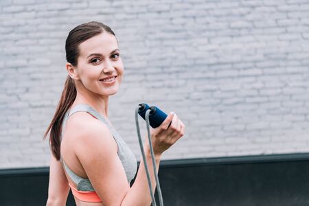 attractive smiling sportswoman holding jump rope on streetの写真素材