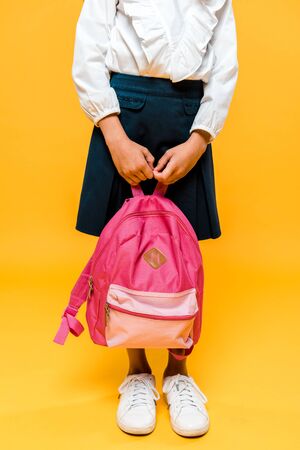 cropped view of schoolkid holding backpack and standing on orangeの写真素材