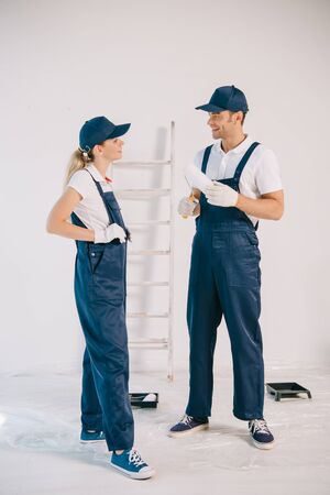 handsome painter in uniform holding paint roller while talking to pretty colleagueの写真素材