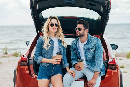 attractive woman and handsome man in denim jackets holding paper cupsの写真素材