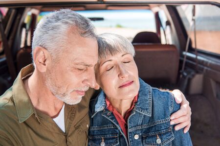 senior couple embracing with closed eyes near carの写真素材