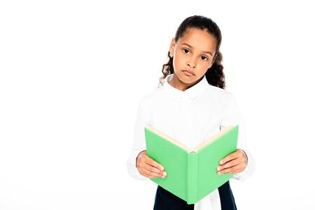 upset african american schoolgirl looking at camera while holding book isolated on white