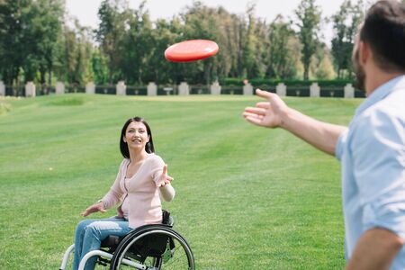 young man throwing flying disc to disabled girlfriend in parkの写真素材