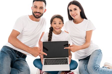 happy parents in white t-shirts pointing with fingers at laptop with blank screen near daughter...