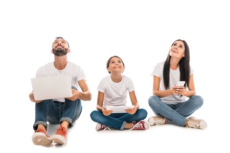 cheerful family sitting with gadgets and looking up isolated on white