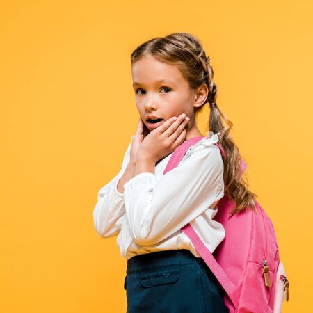 shocked schoolkid touching face and looking at camera isolated on orange
