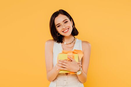 happy smiling girl holding gift box isolated on yellowの写真素材